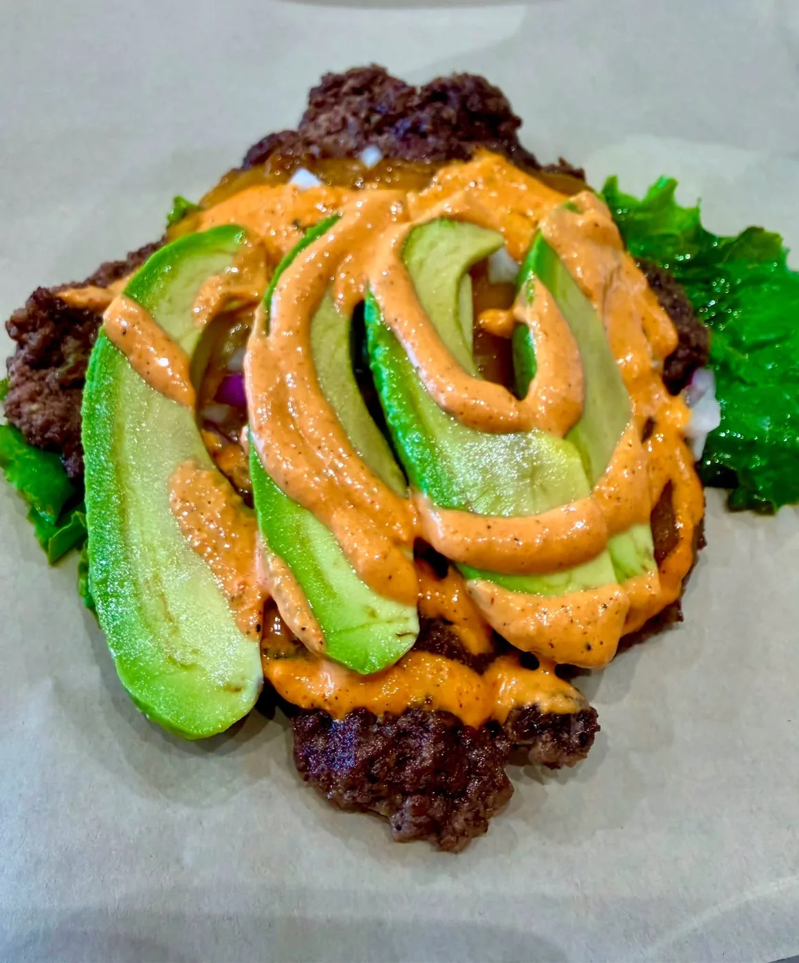Bunless burger on leaf lettuce with avocado slices and a chipotle drizzle