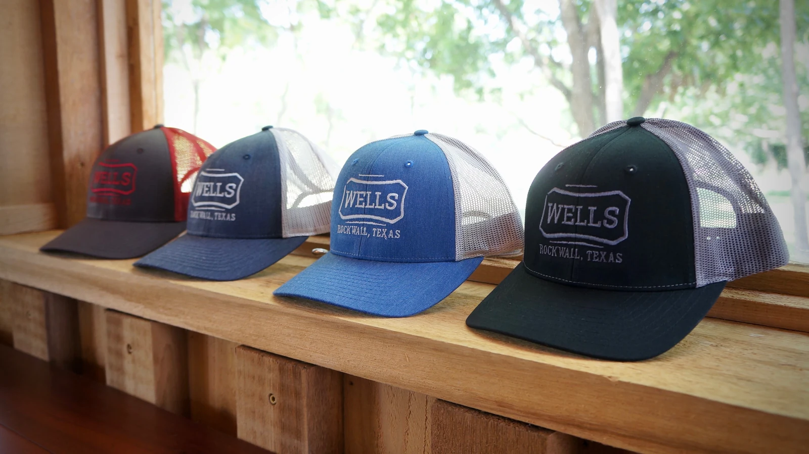 Four Wells Cattle Co. trucker hats lined up on a wooden ledge, each embroidered with the Wells plaque and “Rockwall, Texas”